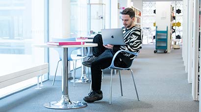 Student sat in a study area looking at a laptop.