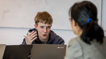 A student and a member of staff having a conversation while working on laptops.
