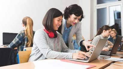 Teacher talking with an asian girl who looking at a laptop.