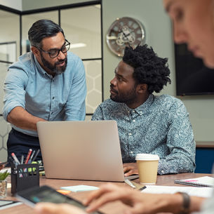 Group of people working around a laptop in an office.