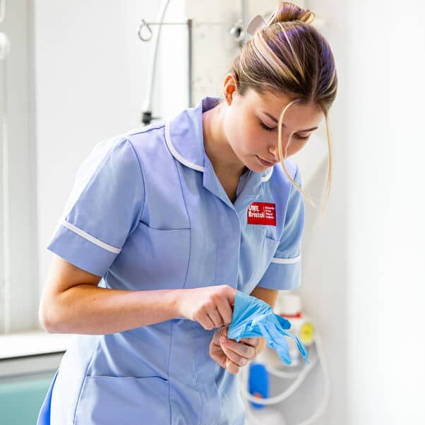 A student nurse putting on blue latex gloves.