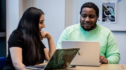 Two students sitting at a table having a discussion with their laptops.
