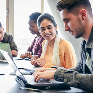 Four students sitting at a table and working on laptops