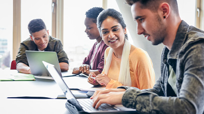 Four students sitting at a table and working on laptops