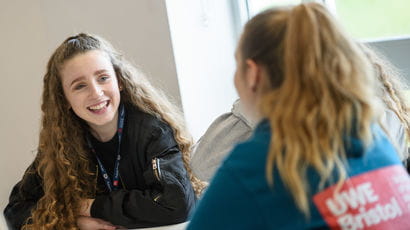 Two females sitting at table having a discussion.