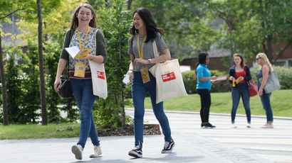 Two females walking, and three females standing in background, at Frenchay campus.