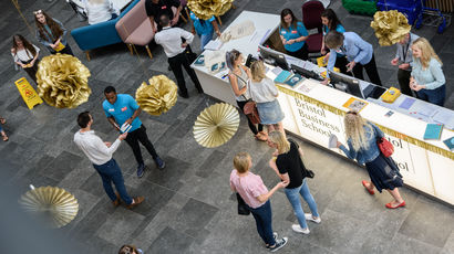 Small groups of males and females standing next to long tables at an event.