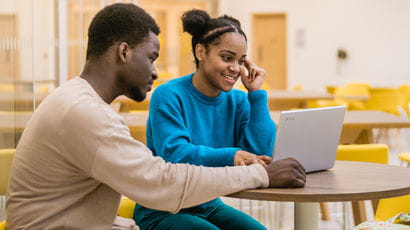 Two people having a conversation while using a laptop.