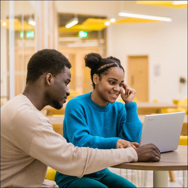 Two people having a conversation while using a laptop.