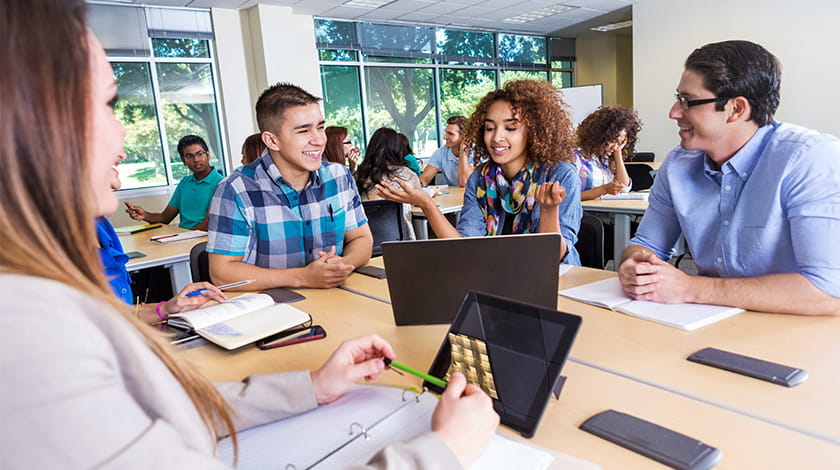 Students sat at a table in a busy classroom smiling and talking.
