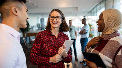 A woman holding a notepad smiling at two students.