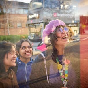 Couple of students smiling whilst looking at the bus timetable at a bus stop.