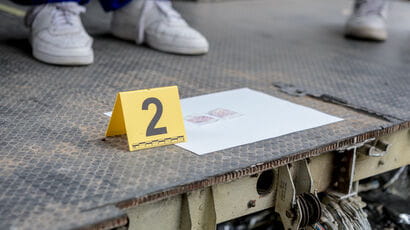 Yellow evidence marker with number 2 sitting on top of a piece of paper with a diagram. Investigators feet in shot.
