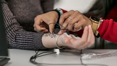 Image of hands with one person attaching cathodes to the other persons wrist and hand.