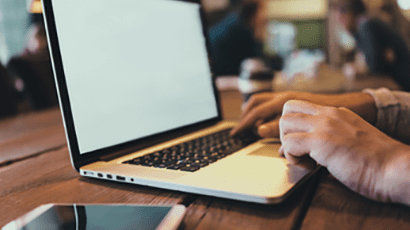 A closeup of someone typing on a laptop with a phone next to them.