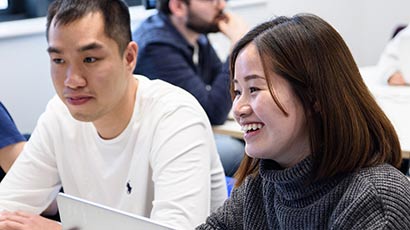 Two students sat at a table in front of a laptop.