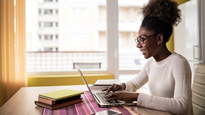 Young woman in white jumper and glasses using laptop at home.