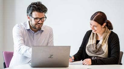 A couple of people sat at a desk looking at a laptop