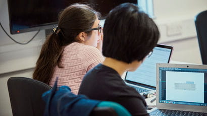 A back to camera shot of two female students working on laptops.