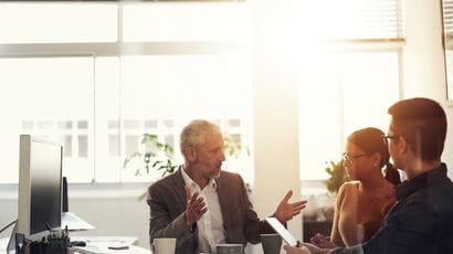 Businessman gesticulating whilst talking to some colleagues at an office desk.