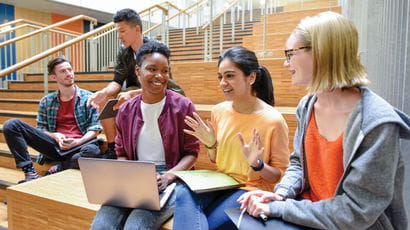 Students sitting on stairs working together on a piece of work with laptops
