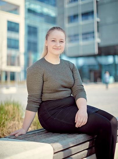 Student Ele smiling at the camera, sat outside the Bristol Business School