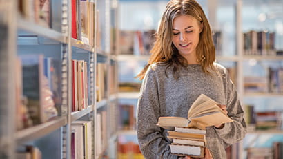 Student looking through pile of books in library