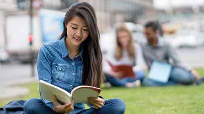 Asian student save on grass reading a book.