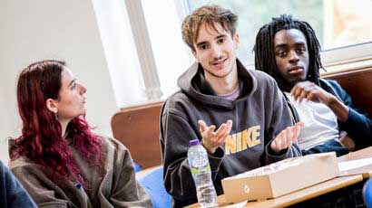 A student gesticulating whilst talking, with a couple of students listening intently either side of him.