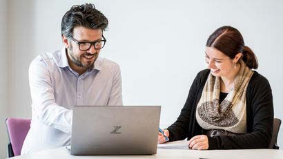 A couple of people sat at a desk looking at a laptop