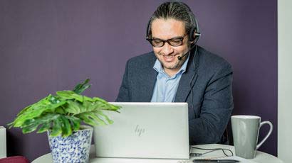 Man talking into a headset looking at a laptop.