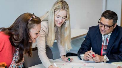 Three people in discussion marking items on some paper.