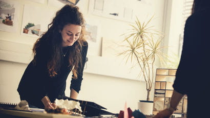 An art student smiling as she does some work with a peer.