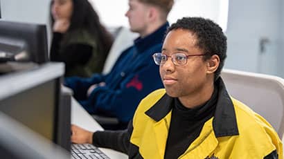 A student looks at a computer screen, sitting at a library workstation.