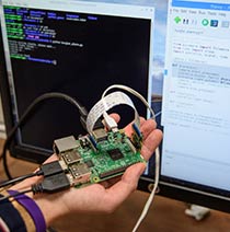 A close up of electrical equipment in front of some computer screens which are displaying code.