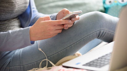 A student sitting in front of a laptop, with a mobile phone