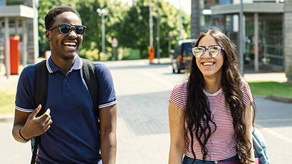 Two students walking along on campus on a sunny day, laughing.