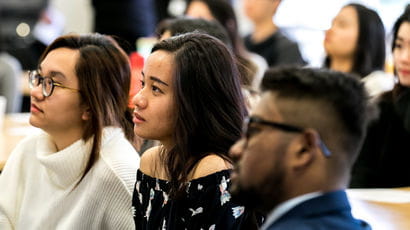 Group of students sat at tables watching a presentation.