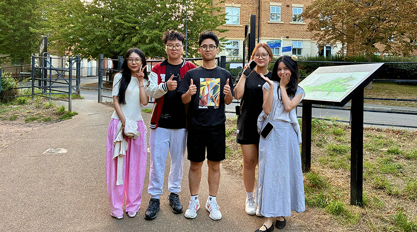 Four students smiling to camera with thumbs up in a green space near Frenchay Campus.