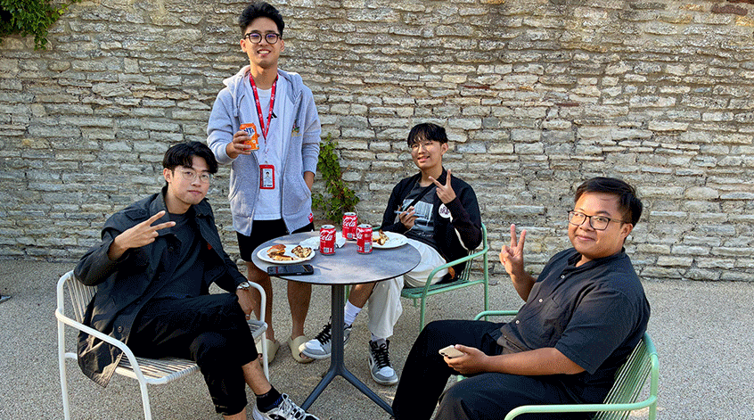 Four international summer school student sat outside around a cafe table in the summer.