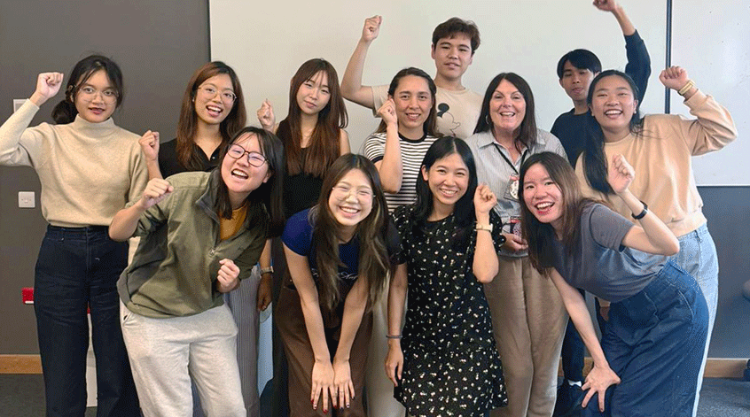 A large group of happy summer school students standing together for a photo, some with the arms in the air.