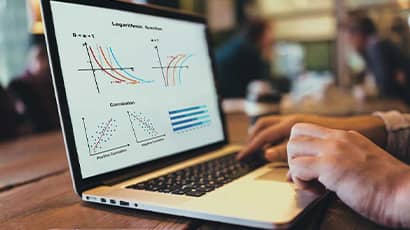 Somebody typing on a laptop with charts and graphs on the screen.