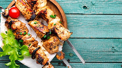 Barbequed meat on skewers against a blue background.