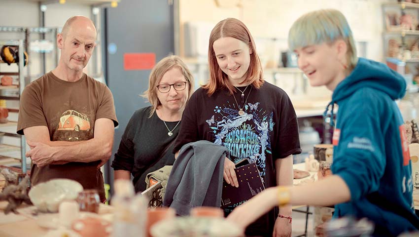 Student showing ceramics to guests at an open day.