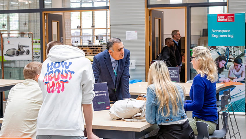 Students and visitors at a large table in the foyer of the Business School talking to a member of staff. 