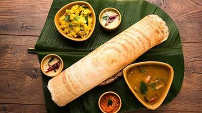 Aerial shot of a rolled dosa with dips and dishes on a banana leaf.