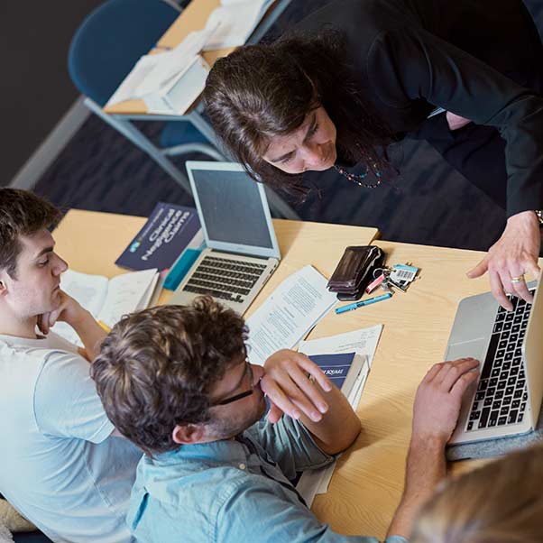 A teacher helping a student and pointing at something on his laptop.