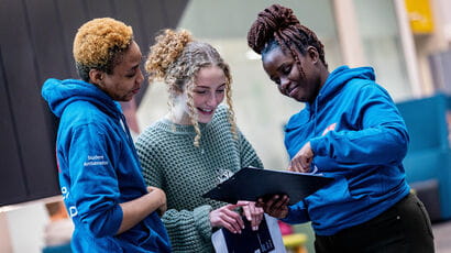 Two student ambassadors chat to a prospective student at an Open Day giving them directions.
