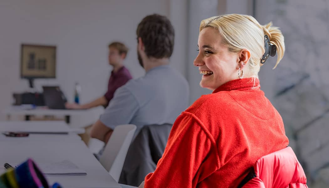 Student smiling in a classroom wearing a red jumper.