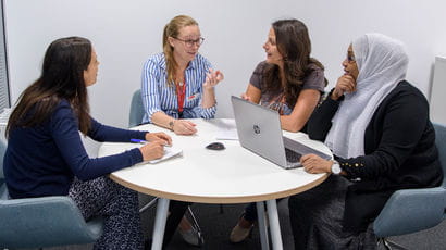 Group of four people sat at a table using a laptop.